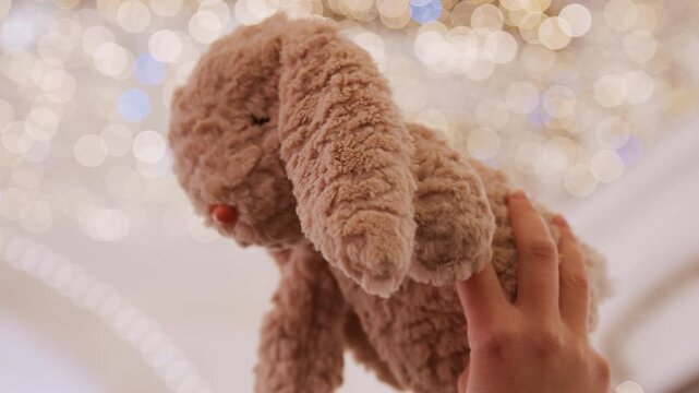 Youngster observes luminous holiday decorations. Tiny child extends hand to bright festive lights. Young child attentively stretches hand towards shimmering holiday ceiling fixtures with curiosity