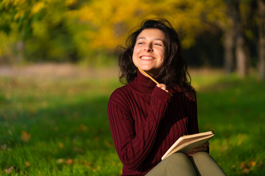 A person write notes sitting on a lawn in an autumn park. Joyful state of mind. Looking for inspiration