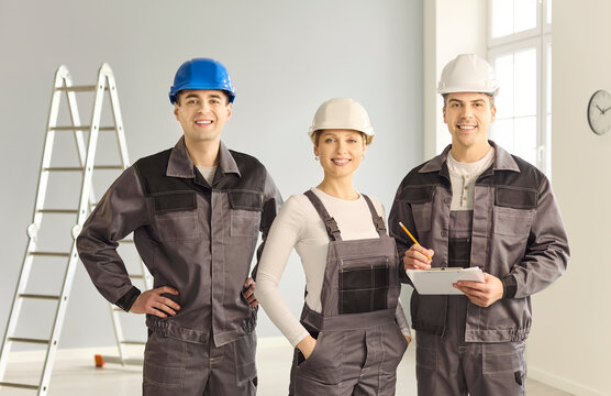 Builders workers team contractors crew renovation. Three smiling pros in gear and helmets stand in a renovated room with clipboard for construction repair. Clear message of teamwork success.