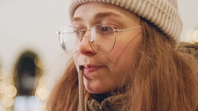White woman tasting seasonal drink under festive lights with straw and glasses surprised reaction captured in closeup food blogger sampling cinnamon chocolate, barista testing recipe, student filming