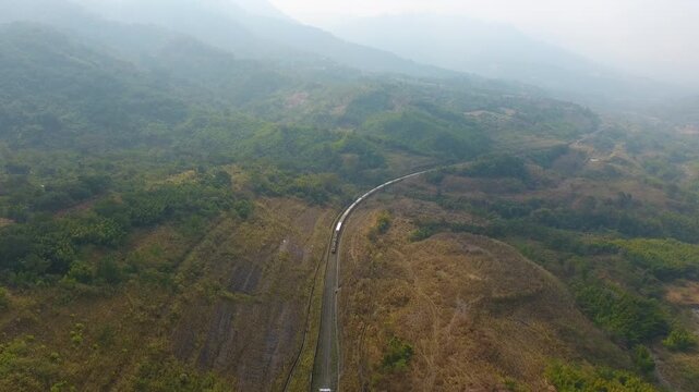 Aerial drone view of a train passing through lush green hills in Haflong, Dima Hasao district, Assam, India
