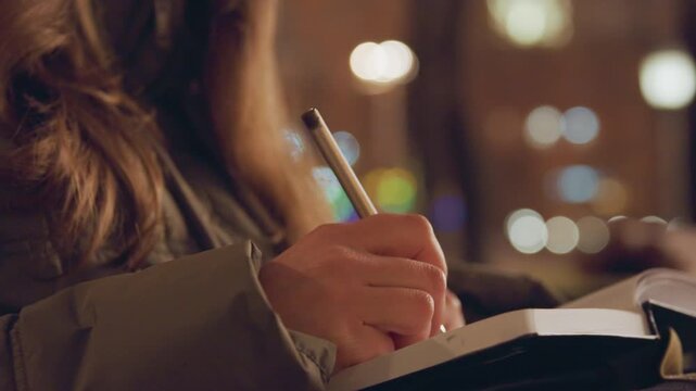 Peaceful woman writes in cafe. Quiet evening at cafe with woman peacefully writing in journal. Tranquil nighttime scene where woman casually records thoughts amid cozy cafe atmosphere