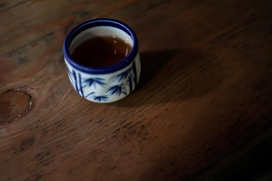 暗い木目テーブルの上の湯呑み。温かいお茶。青い和柄。
