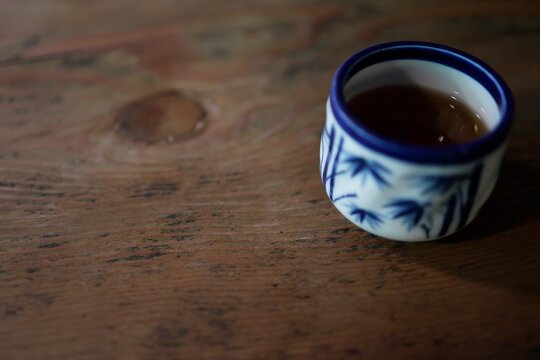 暗い木目テーブルの上の湯呑み。温かいお茶。青い和柄。
