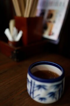 暗い木目テーブルの上の湯呑み。温かいお茶。青い和柄。