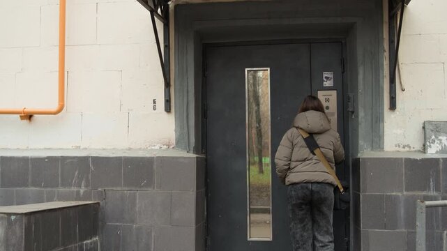Caucasian woman approaching apartment entrance buzzer and door, carrying duffel and backpack in cool evening light resident, delivery driver, commuter and tenant beats as she reaches panel, presses