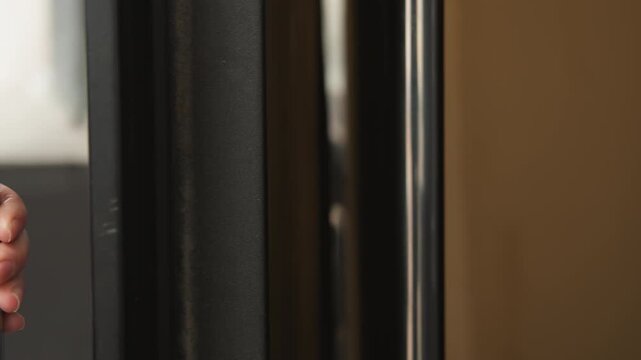 Caucasian hand gripping metal handle on black door thumb pressing against cold chrome, parka sleeve visible, closeup texture of skin and metal, slight motion opening door, urban morning routine