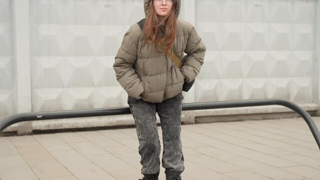 Woman in casual attire gazing upward outdoors. Contemplative woman in puffer coat near bicycle rack outdoor. Urban scene featuring woman in jacket with hands in pockets looking up thoughtfully