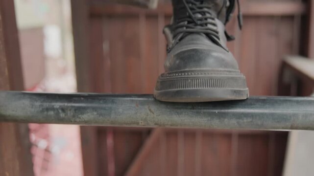 Detailed image capturing rugged footwear stance. Focused shot highlighting textured shoes on city railing. Realistic portrayal of worn boots resting on metallic handrail in urban environment