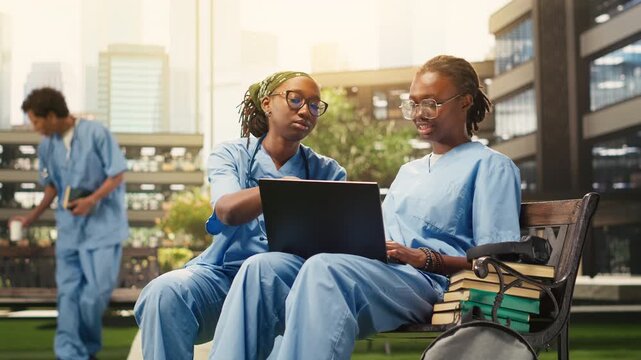 Medical students exchange ideas with a laptop and notes during outdoor group study on a campus bench, combining medical training, peer tutoring and collaborative learning for healthcare education.
