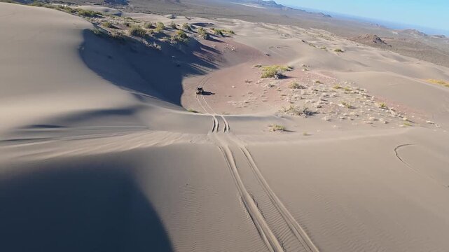 Dynamic aerial FPV view of off road 4WD vehicle driving through sand dunes landscape