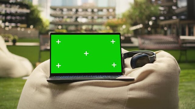 The laptop shows a green screen mockup on an outdoor beanbag with headphones, creating an editable screen asset for education and technology content.