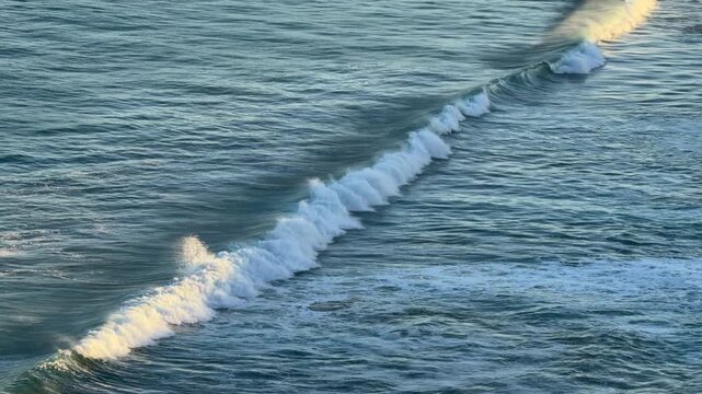 Tracking shot over blue ocean waves building and breaking in later afternoon light in 4k footage