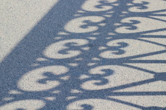 The shadow of the lacy fence on the asphalt makes for a beautiful artistic photo on a summer day &mdash; light and shadow