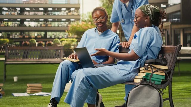 Diverse medical students learn together from coursework during group study on a campus bench, with classmates sharing notes and preparing for a medical training program in an outdoor academic setting.