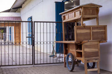 Traditional empty wooden street food vendor cart parked outside a closed metal gate. © FdaxssPhotos