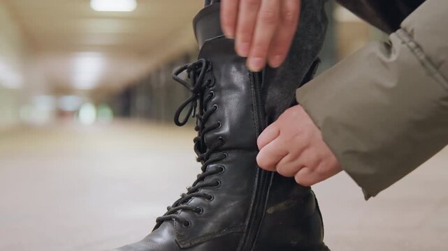 Person fastening shoes in quiet tunnel. Intimate shot of hands securing footwear in winter tunnel. Close shot capturing hands lacing boots amidst winter commute setting with blurred background