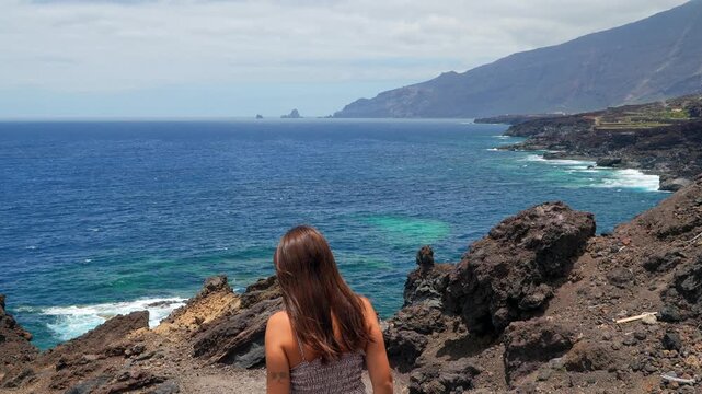 Young woman enjoying freedom on a volcanic cliff overlooking the ocean