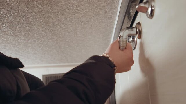 Visitor carefully locks door. Suspenseful evening with cautious visitor securing hallway entrance. Visitor in jacket cautiously secures hallway door with precise effort and minimal sound