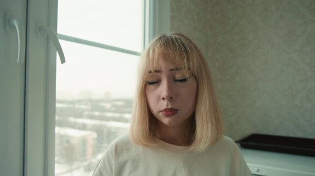 Woman tasting lemon near window, grimace and thumbs down, cooking taste test, home kitchen ambiance, candid vlogstyle frame, cold winter cityscape outside, natural soft light, unsatisfied flavor