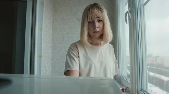 Blonde woman at refrigerator scanning for ingredients and planning simple recipe, soft daylight, kitchen counter and patterned glass, thoughtful domestic routine and budget meal prep