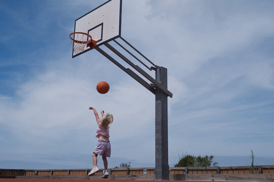 Blonde Toddler Girl Jumping to Shoot a Ball on an Outdoor Basketball Court