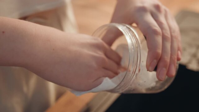 Cleaning glass jar. Removing water droplets from glass container with gentle circular wipes. Thoroughly cleaning glass jar interior using careful circular motions and soap suds rinsing process