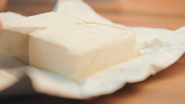 Butter slicing technique. Preparing butter for baking. Detail of butter being sliced on wooden surface. Closeup of hands dividing chilled butter block on wooden cutting board for recipes