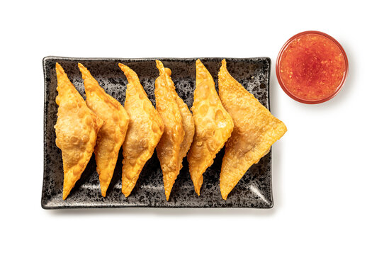Top view of delicious deep-fried golden wontons served on black ceramic plate with side of sweet chili dipping sauce, isolated on white. Perfect for Asia appetizer and snack menu concepts.