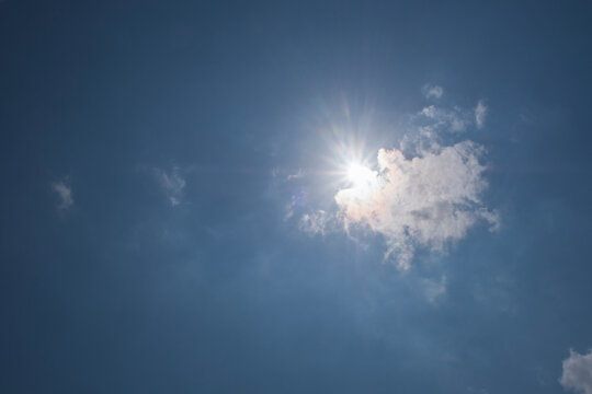 Bright sunburst shining through a fluffy white cloud against a clear blue sky. Natural light and atmospheric contrast create a peaceful background for weather and nature concepts