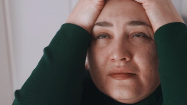 White woman in intense facial pain and grimace, extreme closeup captures tearful eyes, clenched jaw, hands pressing temples, raw suffering and sensitivity to light, home interior background hints