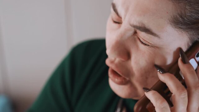 White woman calling emergency services with strained voice and tearful expression, closeup on ear and phone, long nails gripping device, urgent whispered conversation with dispatcher interior
