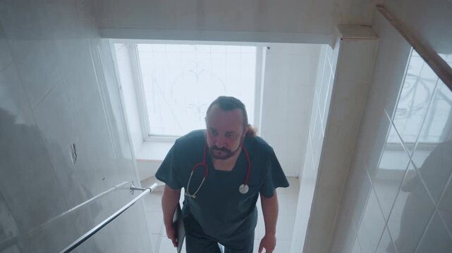 White paramedic climbing narrow tiled staircase, stethoscope visible and steady ascent, approaching skylight window while carrying kit, scanning ceiling and checking access, communicating over radio,