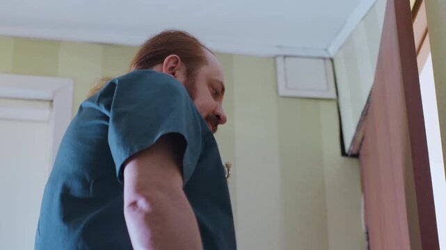 White medic assessing patient chart and vitals, red hair clinician in teal scrubs with stethoscope studies clipboard in doorway, concentrated indoor scene showing professional home visit evaluation