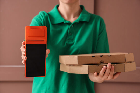 Delivery person in green polo shirt holding pizza boxes and payment terminal for contactless transaction, the terminal is extended forward for a contactless transaction