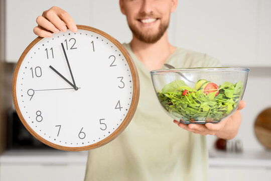 Smiling man holding a clock and a fresh green salad, healthy eating habits and time management for wellness