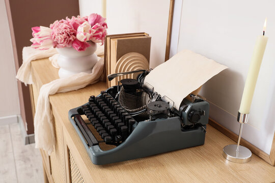 Vintage typewriter, books and vase with tulips on commode in office