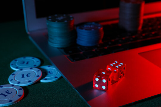 Laptop with poker chips and dices on green table, closeup