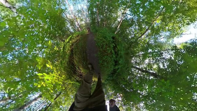 Tiny-planet extreme wide angle view of a man and his dog walking along a narrow trail through a green summer forest
