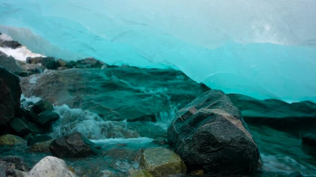 Close-up footage filmed inside a crevice beneath Nigardsbreen Glacier in Norway. Meltwater drips and flows through the ice, revealing the vivid blue tones and textured interior of the glacier as it sl