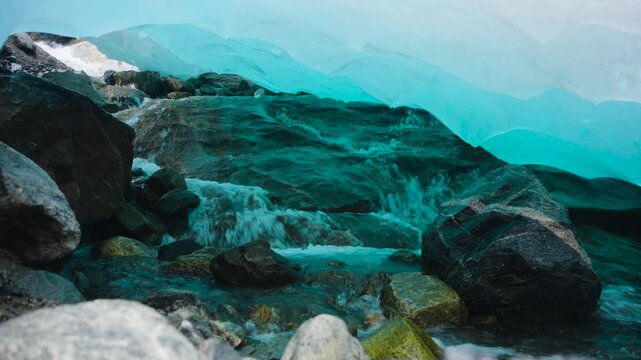 Close-up footage filmed inside a crevice beneath Nigardsbreen Glacier in Norway. Meltwater drips and flows through the ice, revealing the vivid blue tones and textured interior of the glacier as it sl