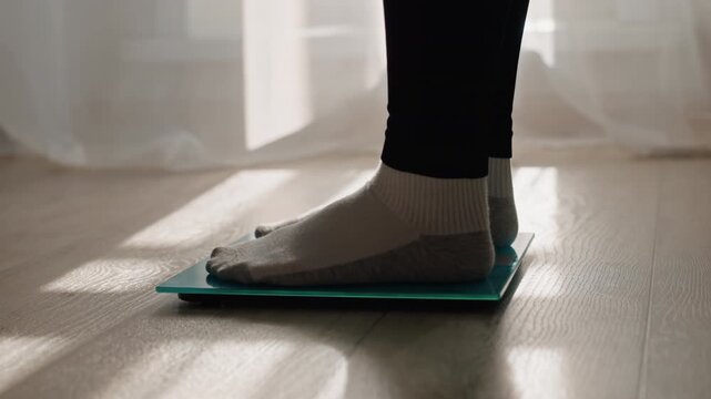 Sunlit home weighin on glass scale by sheer curtain, socked feet pause on digital scale as warm light and shadows fall across hardwood floor, quiet contemplative mood, mindful tracking of weight