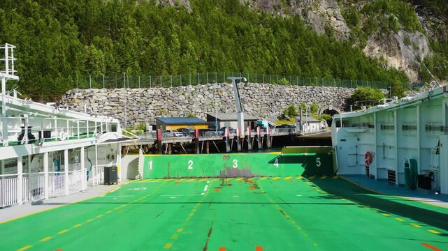 Static view from the deck of a Norwegian ferry as it departs from the port. The ferry appears almost motionless in the frame while the shoreline and harbor structures gradually shift in the background