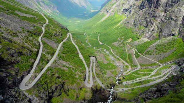 Aerial view of Trollstigen, the famous mountain road in Norway, winding through a steep green valley. The camera slowly moves forward and rises, revealing the dramatic scale of the serpentine road