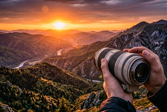Hands holding a large telephoto camera lens against a stunning mountain landscape during sunset