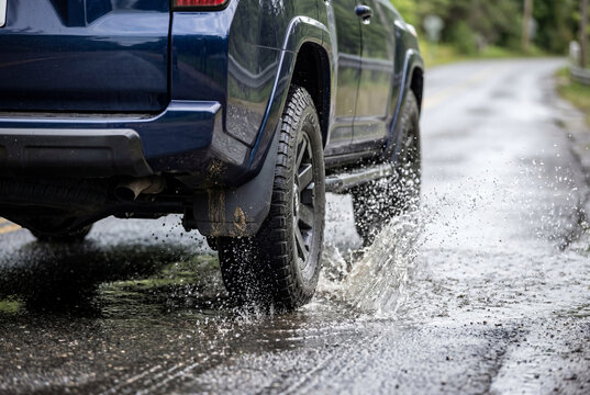 Rear wheel of a dark blue suv driving through a wet puddle and splashing water on the road