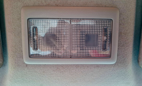 Frontal close-up view of a dual-lens overhead dome reading light fixture mounted on a car ceiling fabric roof liner.