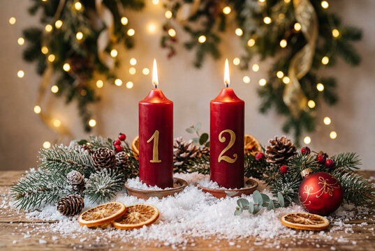 Two lit red advent candles numbered one and two on snow surrounded by festive fir branches