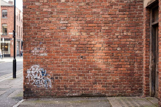 Weathered red brick wall texture with doorway in urban alley