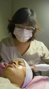 Cosmetologist using high frequency machine on woman's face